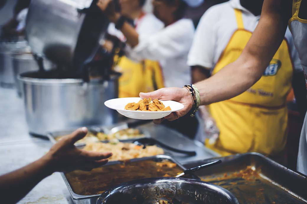 Volontario porge piatto di cibo in una mensa per i poveri